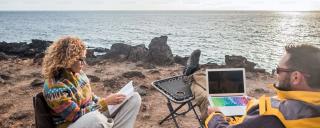 Banner für Blogbeitrag zu Workation zeigt zwei Personen, die am Strand arbeiten