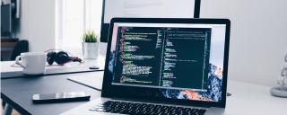 Banner für Blogbeitrag zeigt Laptop auf Schreibtisch mit Programmiercodes